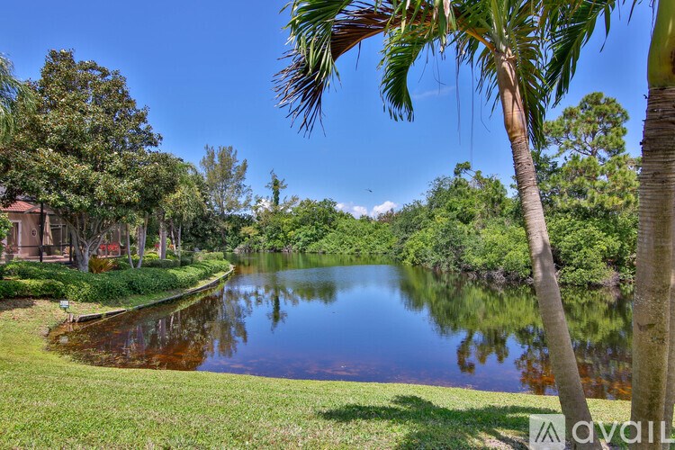 A serene landscape with a lake, palm trees, and a house in the background.