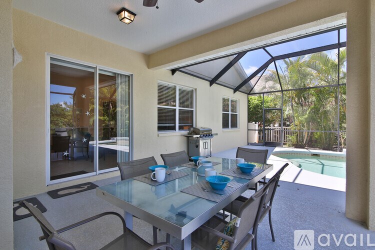 A glass table with chairs is set up on a patio with a pool in the background.