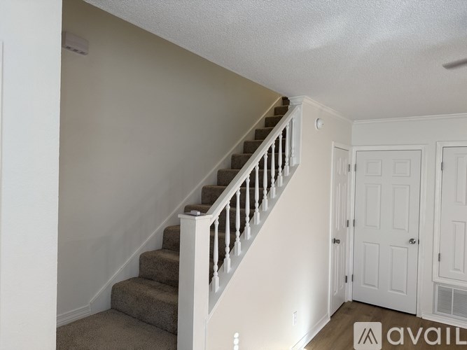 A staircase with a carpeted runner and white balusters leads up to a white door.