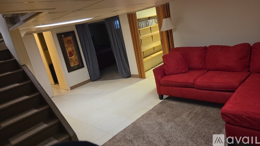 A red couch is placed in a room with a staircase on the left side.