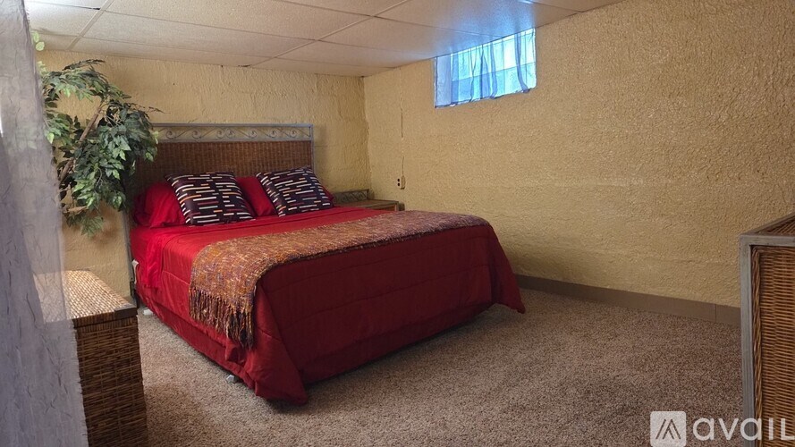 A bedroom with a red bedspread and pillows, a window with a blue curtain, and a wall-mounted TV.