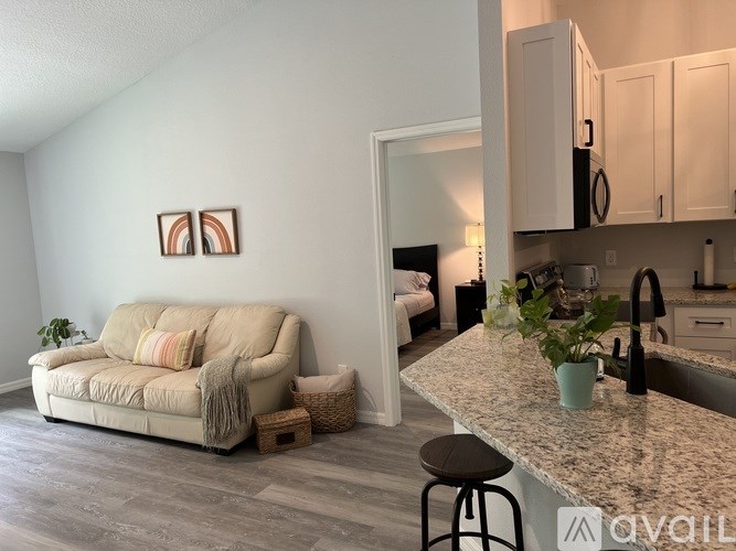 A living room with a beige couch and a kitchen area with white cabinets.
