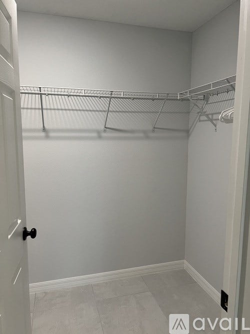 A white door with a black handle is open to a white hallway with a white tiled floor and a white wall with a white shelf above it.