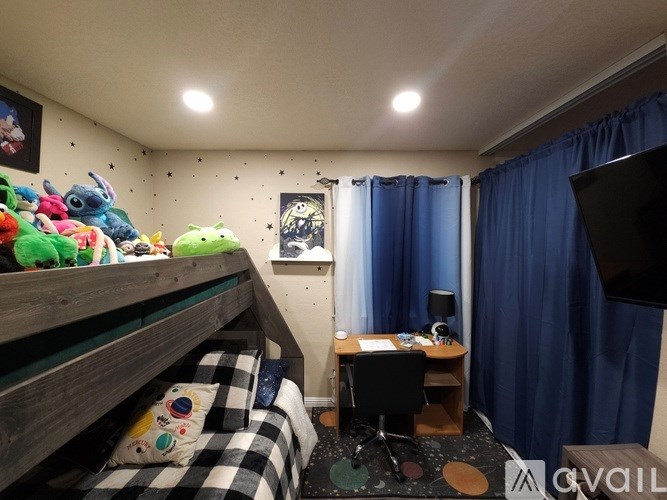 A room with a bunk bed, a desk with a chair, and a window with blue curtains.