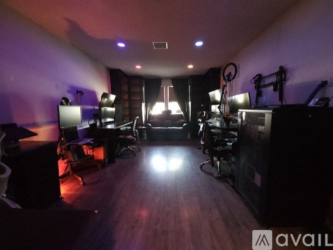A dimly lit room with a desk, chairs, and computer equipment.
