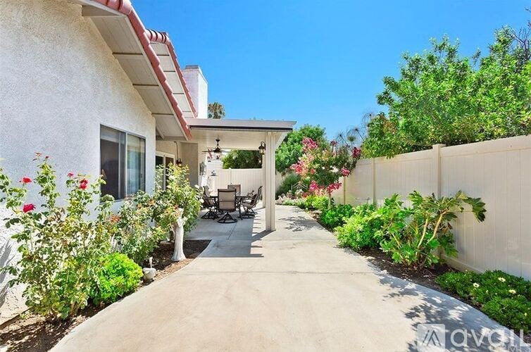 A white house with a red roof and a patio with chairs and plants.