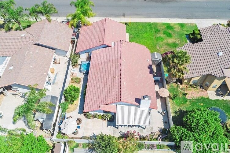 A house with a red roof is surrounded by trees and other houses.