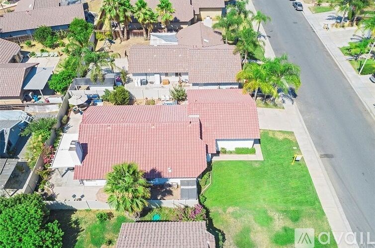 A house with a red roof is surrounded by other houses and trees.