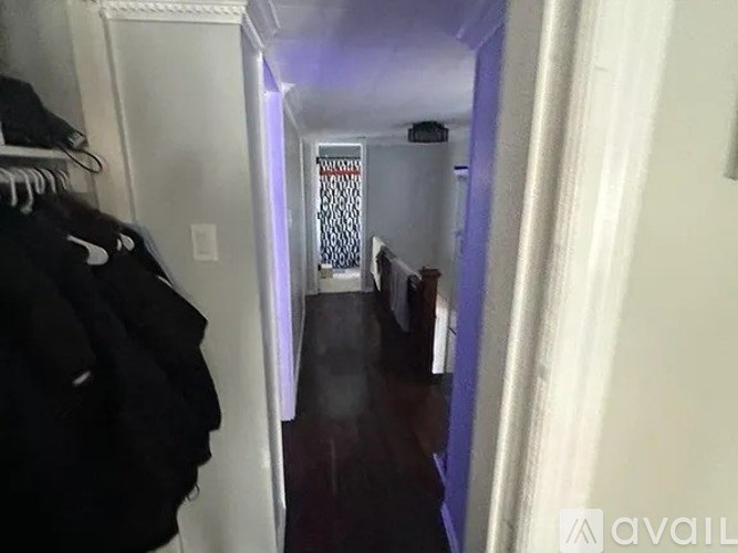 A hallway with a row of clothes hanging on the left and a door at the end.