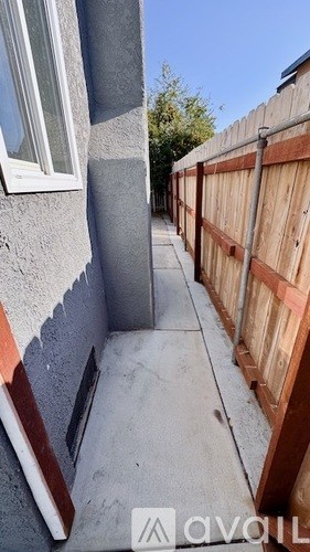 A narrow alley with a wooden fence on one side and a grey wall on the other.