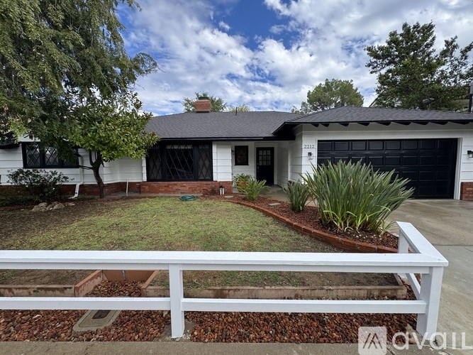 A white house with a black garage door and a white fence.