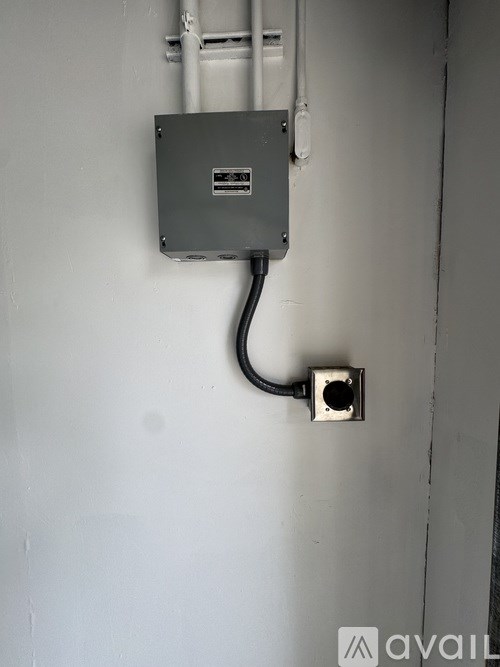 A grey box is attached to a white wall with a black cable.