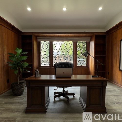 A wooden desk with a laptop and a chair in front of a window.