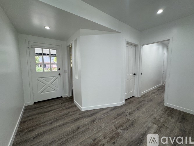 A room with white walls and a wooden floor with a door on the left side.