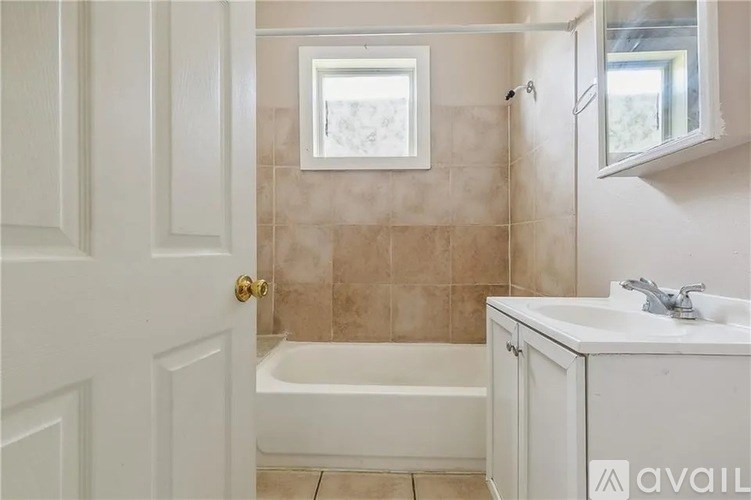 A bathroom with a white door, a bathtub, a sink, and a window.