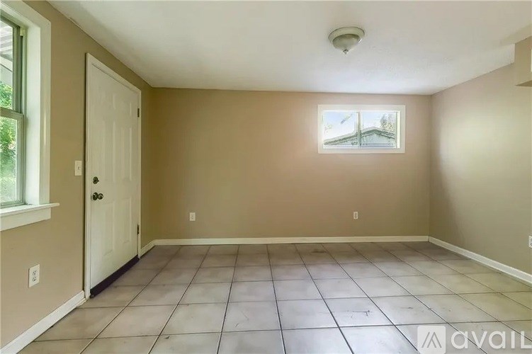 A room with a window showing a view of a tree and a door on the left.