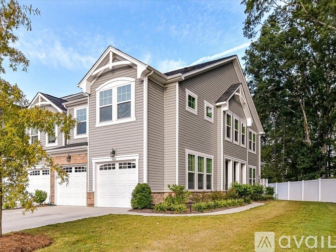 A house with a grey siding and white garage doors is surrounded by greenery.