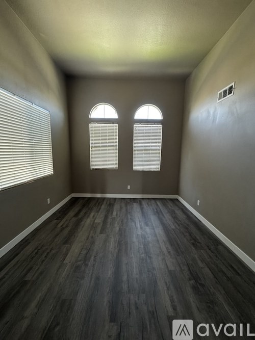 A room with wooden flooring and two windows with blinds.