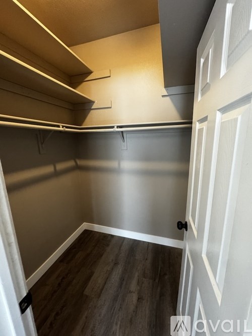 A white door is on the right of a room with a grey wall and a wooden floor.