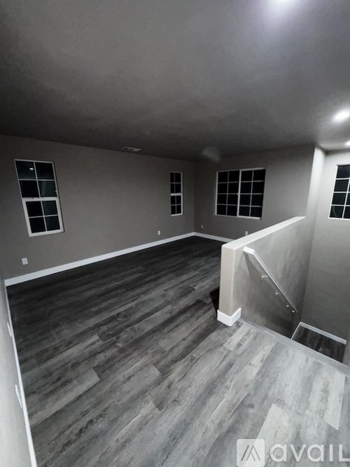 A room with wooden flooring and three windows.