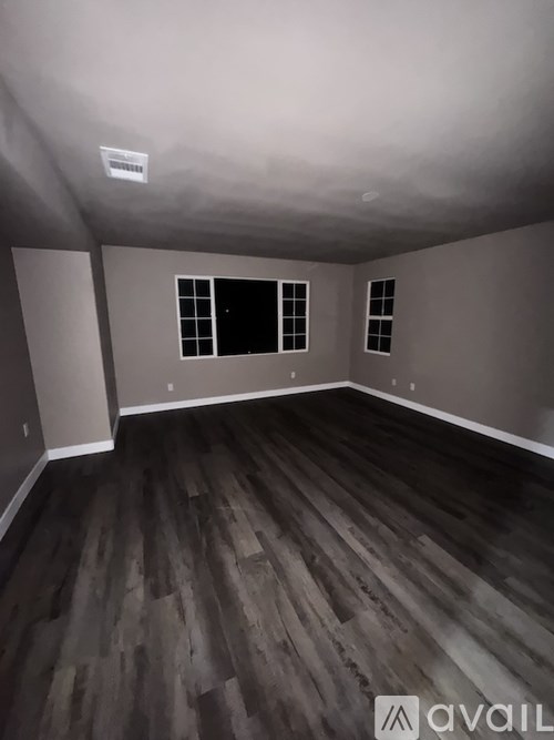A room with wooden flooring and two windows.