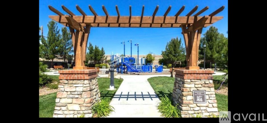 A wooden archway with a plaque underneath it stands in front of a playground.