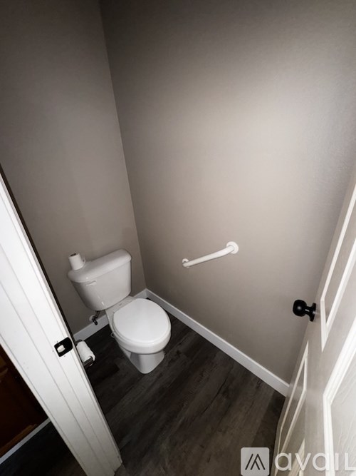 A white toilet with a white grab bar in a bathroom.