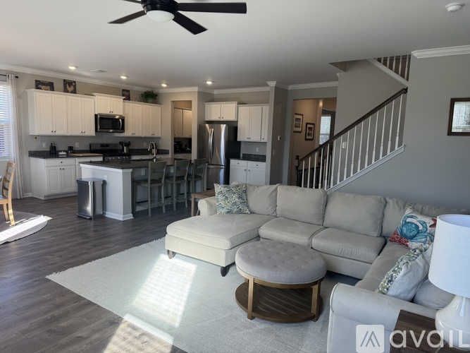A well-lit, spacious kitchen and living room with a grey sofa and a white rug.