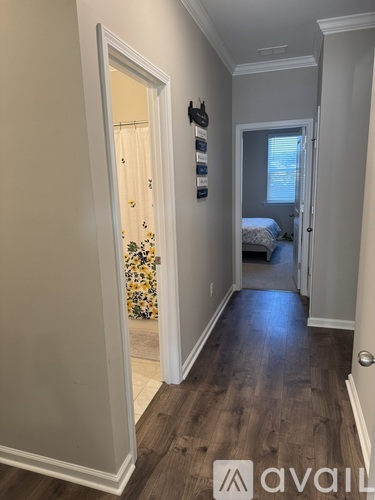 A hallway with a door on the left and a bedroom with a bed and window on the right.