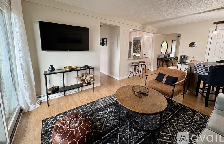 A living room with a black and white rug, a wooden coffee table, and a flat screen TV mounted on the wall.