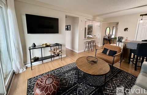 A living room with a black and white rug, a wooden coffee table, and a flat screen TV mounted on the wall.