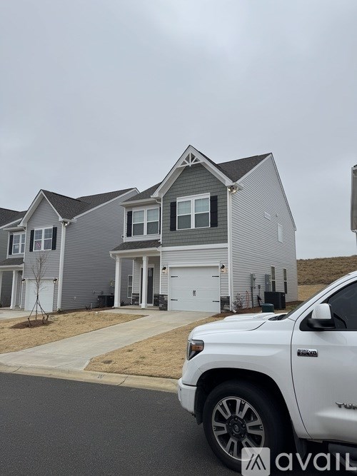 A white pickup truck is parked in front of a grey house.