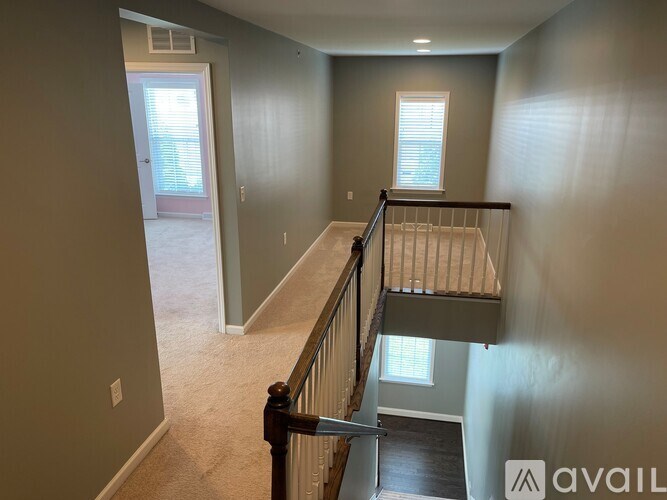 A hallway with a carpeted floor, a staircase with a railing, and a doorway leading to another room.