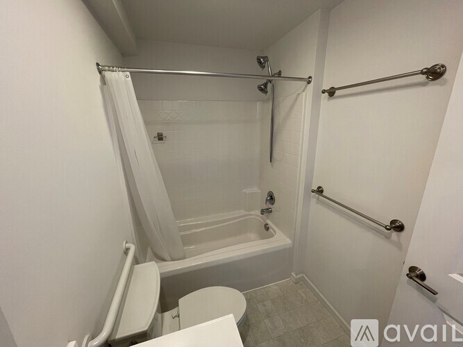 A white bathroom with a toilet, tub, and grab bars.