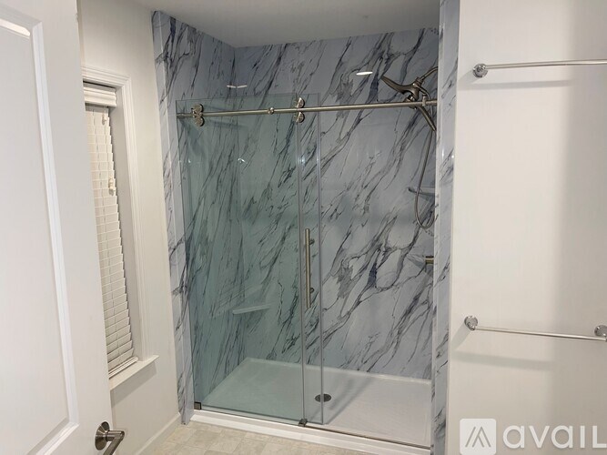 A bathroom with a marble shower wall and a glass door.