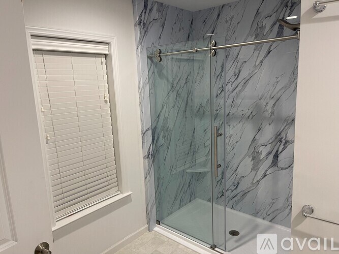 A bathroom with a marble shower and a window with blinds.