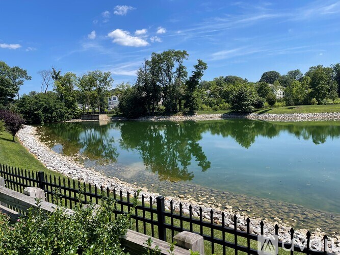 A serene park with a pond, trees, and a wooden fence.