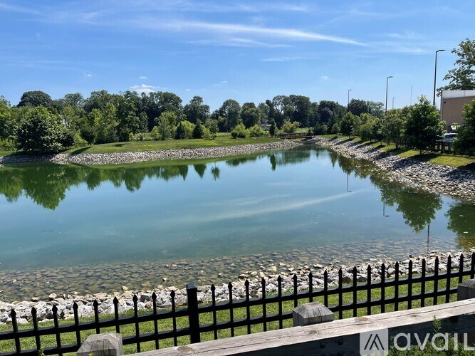 A calm lake with a black fence in the foreground and a building in the distance.