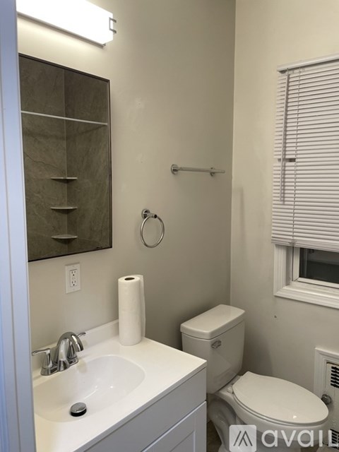 A bathroom with a toilet, sink, mirror, and window.