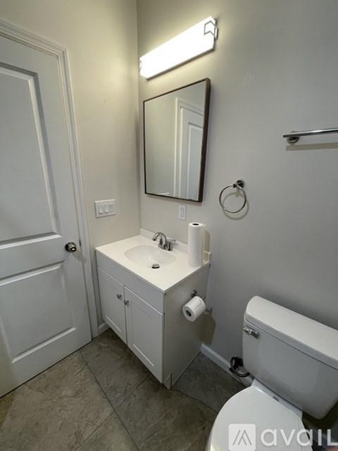 A bathroom with a toilet, sink, mirror, and light.
