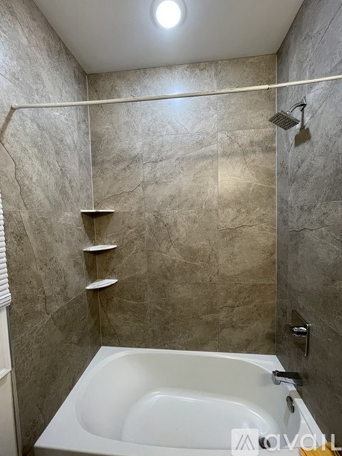 A bathroom with a white bathtub and grey tiled walls.