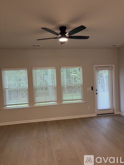 A room with a ceiling fan and three windows with blinds.