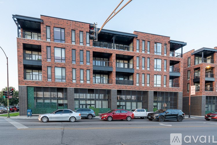 A red brick building with a crane on the top floor and cars parked in front.