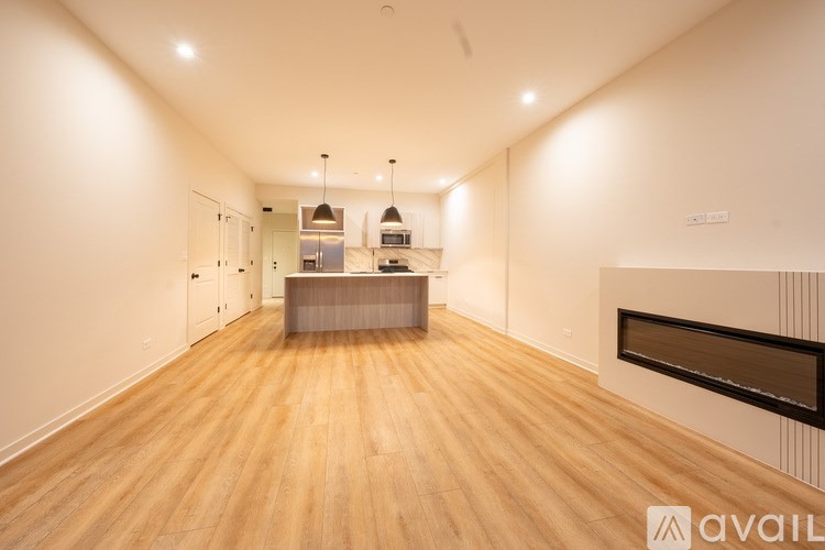 A spacious room with wooden flooring and a kitchen area in the background.