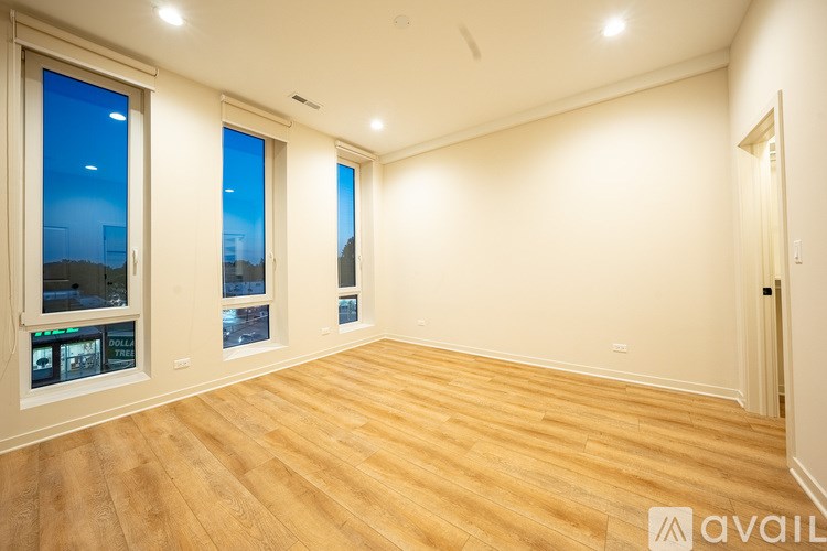 A spacious room with wooden flooring and three windows.