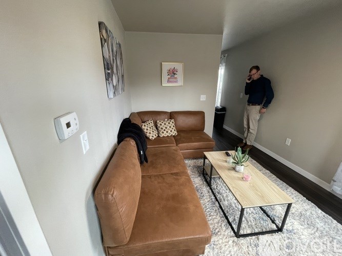 A man stands in a living room with a brown couch and a coffee table.