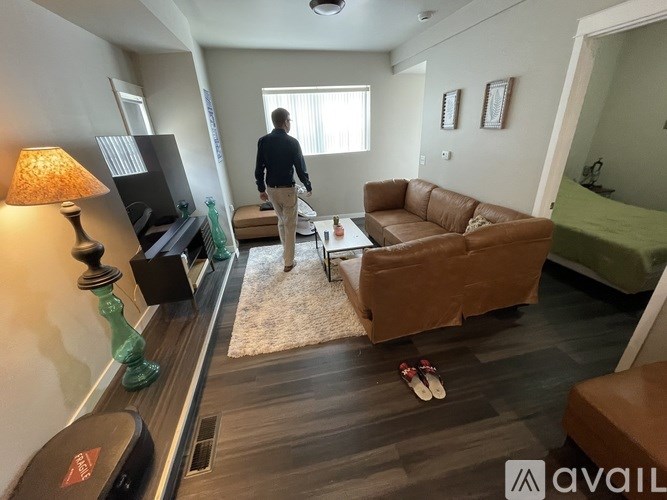 A man is walking through a living room with a brown couch and a rug.