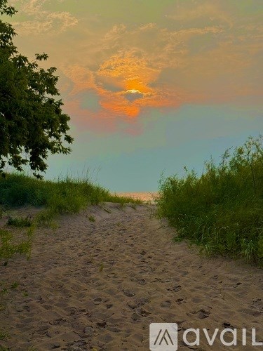 A beach scene with a path leading to the ocean at sunset.