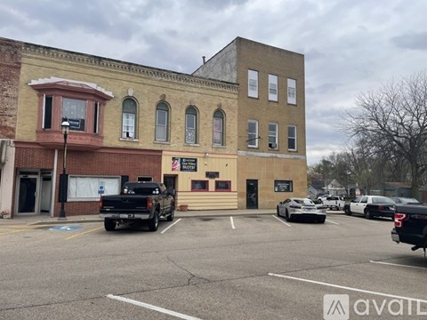 A parking lot with cars and a building with a sign that says "AVAILABLE".