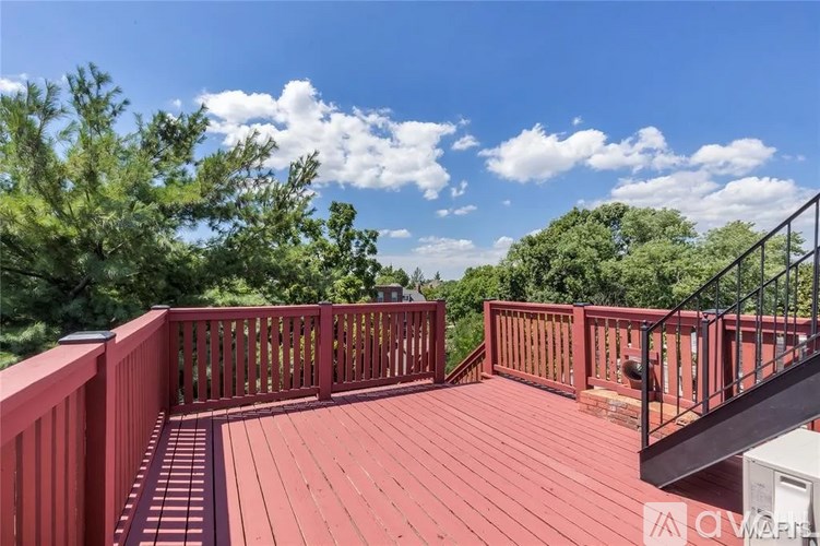 A wooden deck with a metal railing and stairs leading to a house.